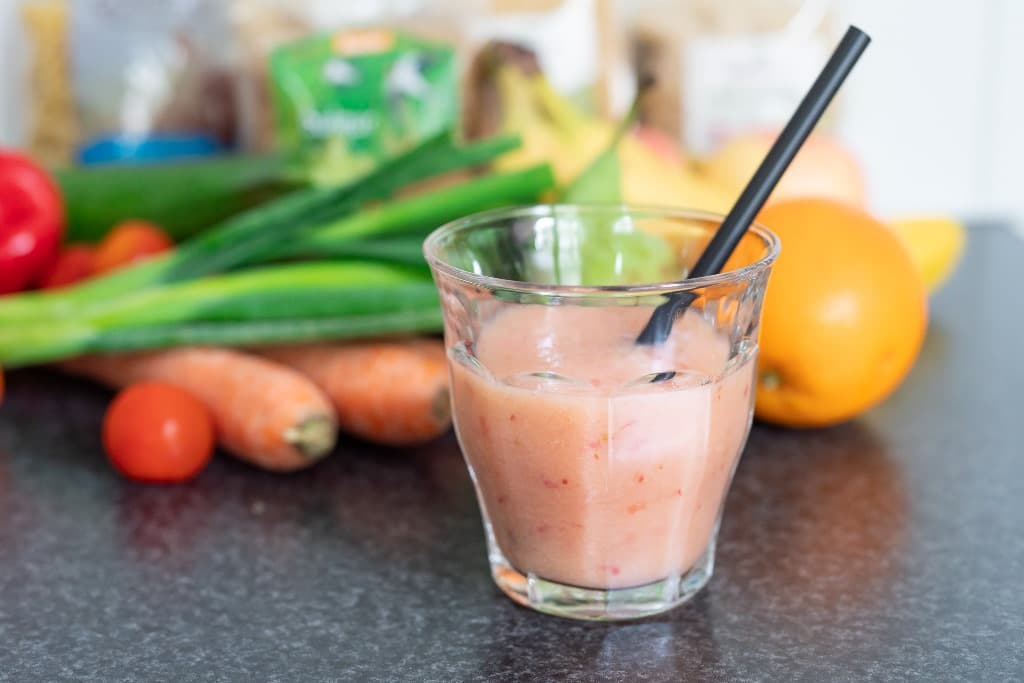 Een glas fruitsmoothie met verse groente en fruit op de achtergrond