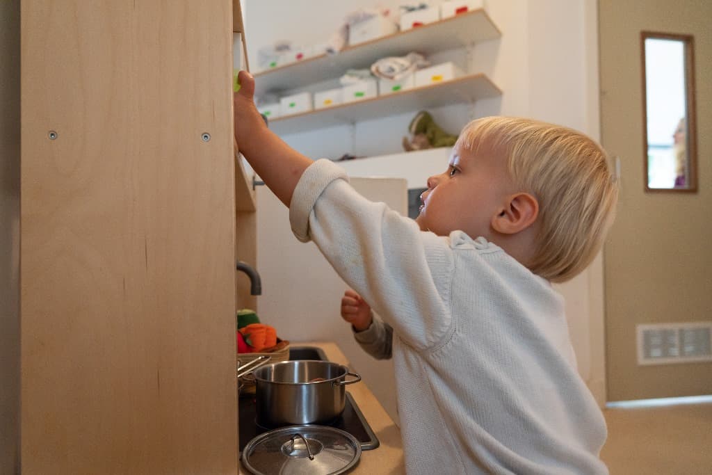 Een peuter pakt iets uit het kastje van de speelkeuken
