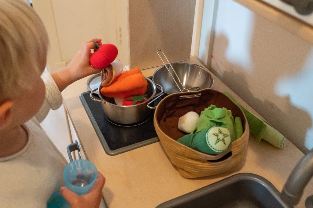 Een kind kookt met speelgoedgroente in de speelkeuken